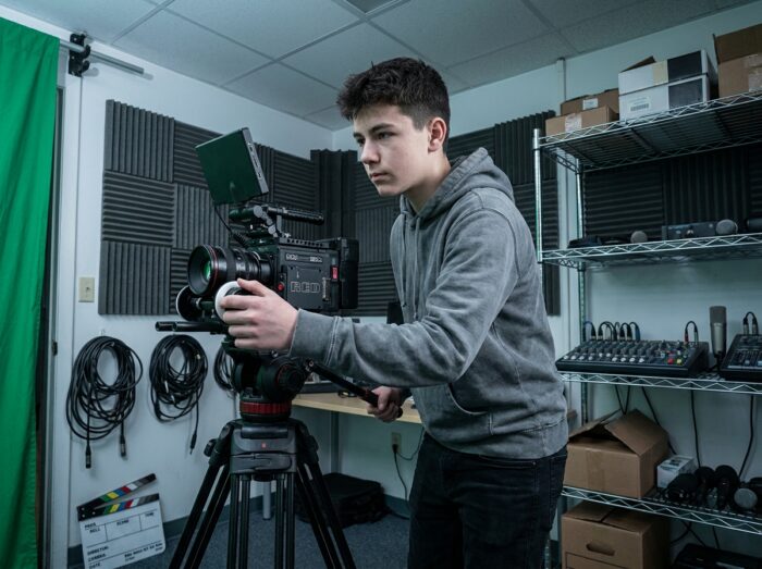 Adolescent utilisant une caméra professionnelle dans un studio vidéo scolaire pour se former aux métiers du cinéma