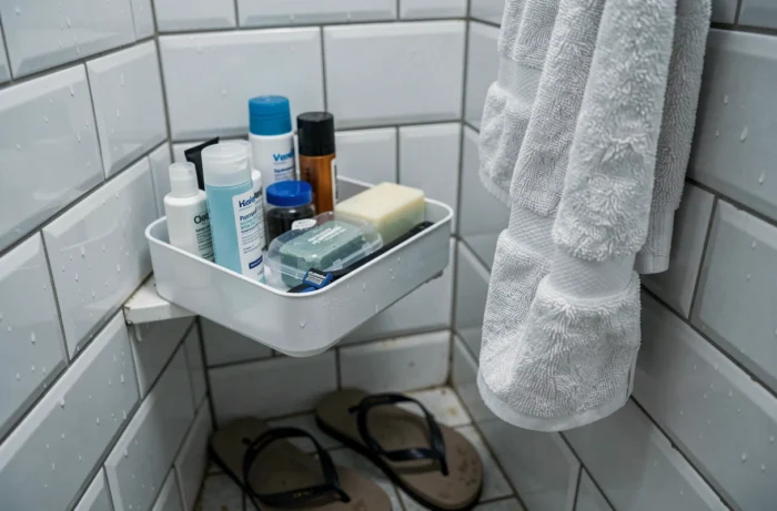 Panier de douche organisé avec produits de toilette et tongs dans une cabine de douche partagée en auberge